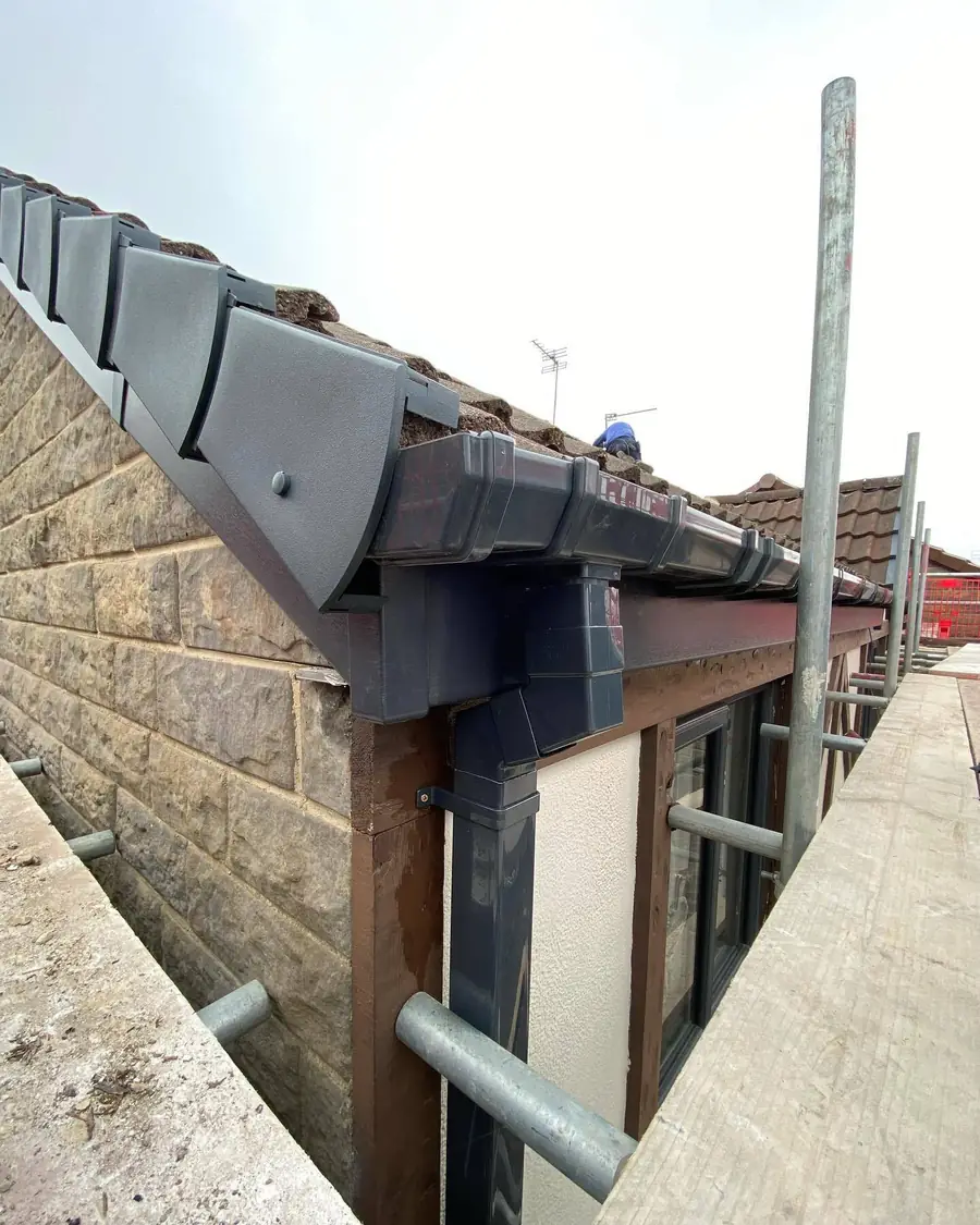 Black gutter and fascia fitted along a stone house, scaffold up