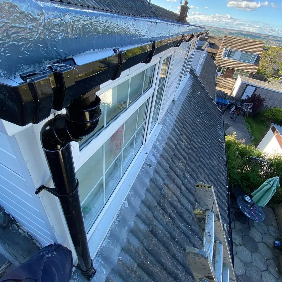 Black gutter and downpipe above a conservatory roof