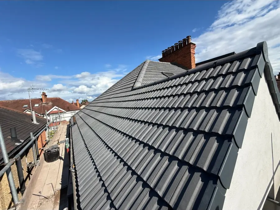 New dark grey interlocking tiles along a gable verge, chimney stack at the far end