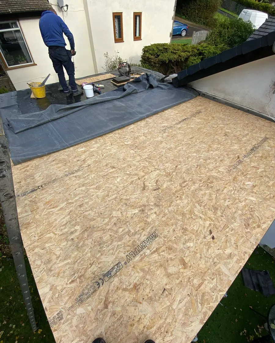 New flat roof deck boards laid over the joists, roofer working beyond