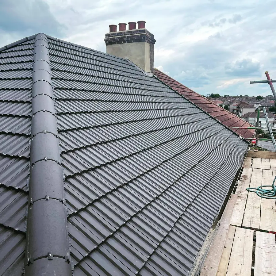Grey tiled pitched roof with a dry ridge, chimney and scaffold boards along the eaves