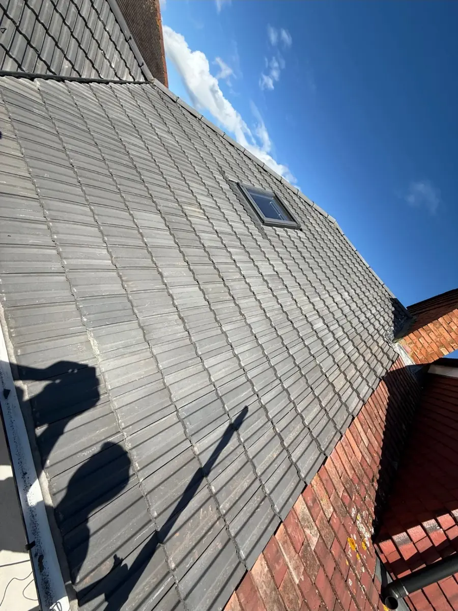 Grey tiled roof slope with a roof window against a clear blue sky