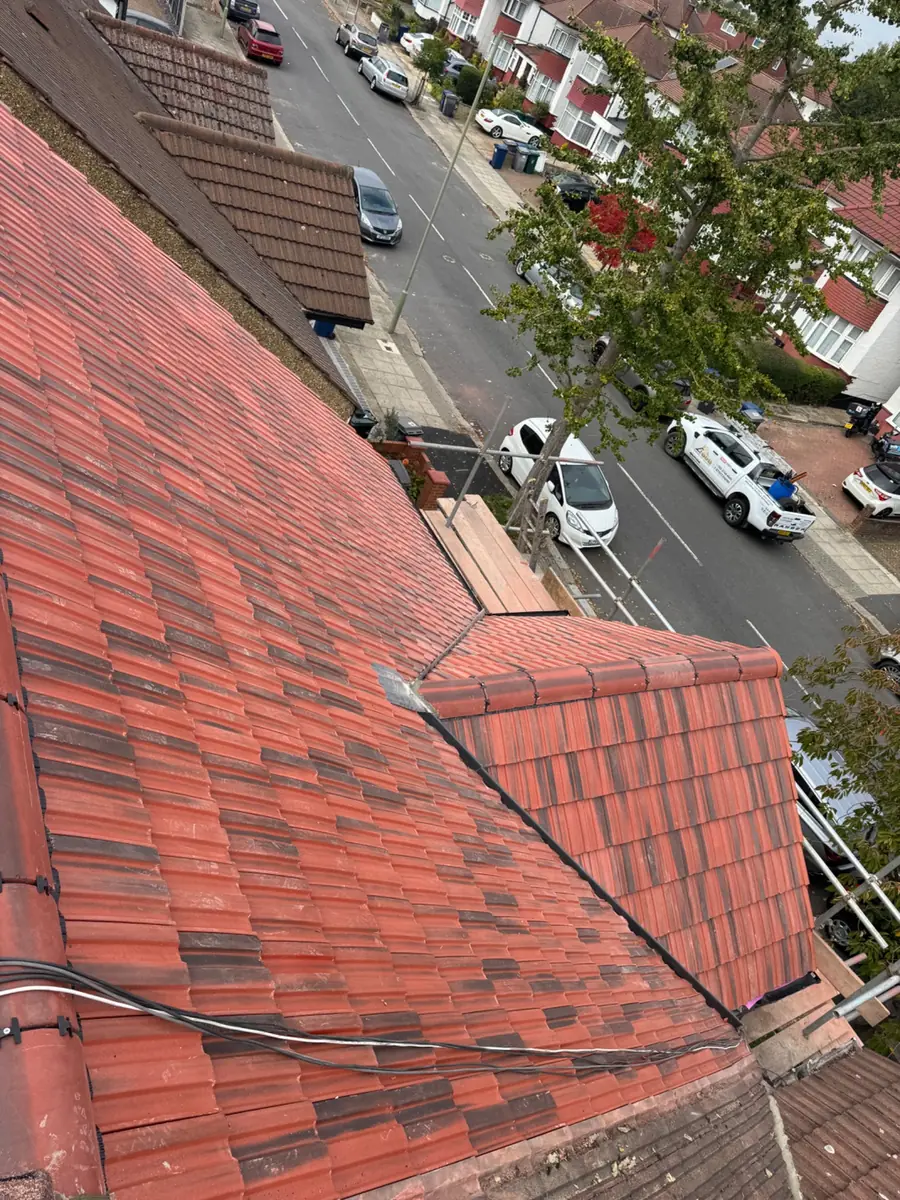 Red tiled roof slope and hip from above, looking down to a tree-lined road