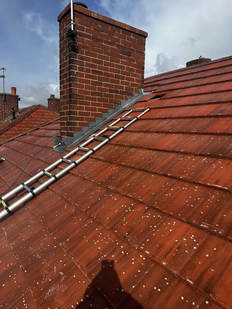 Red tiled roof with a brick chimney and a roof ladder hooked over the ridge