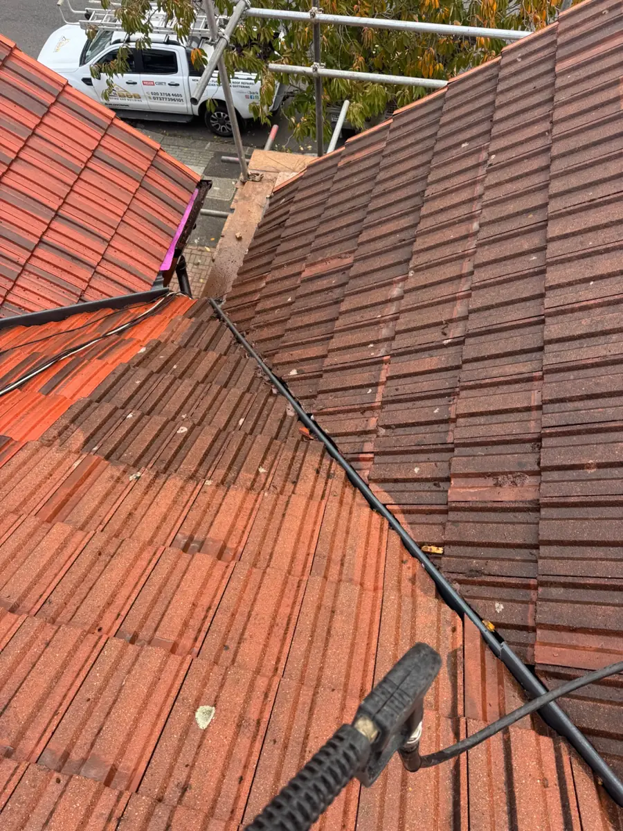 Red tiled roof being cleaned with a pressure washer lance to clear moss and dirt