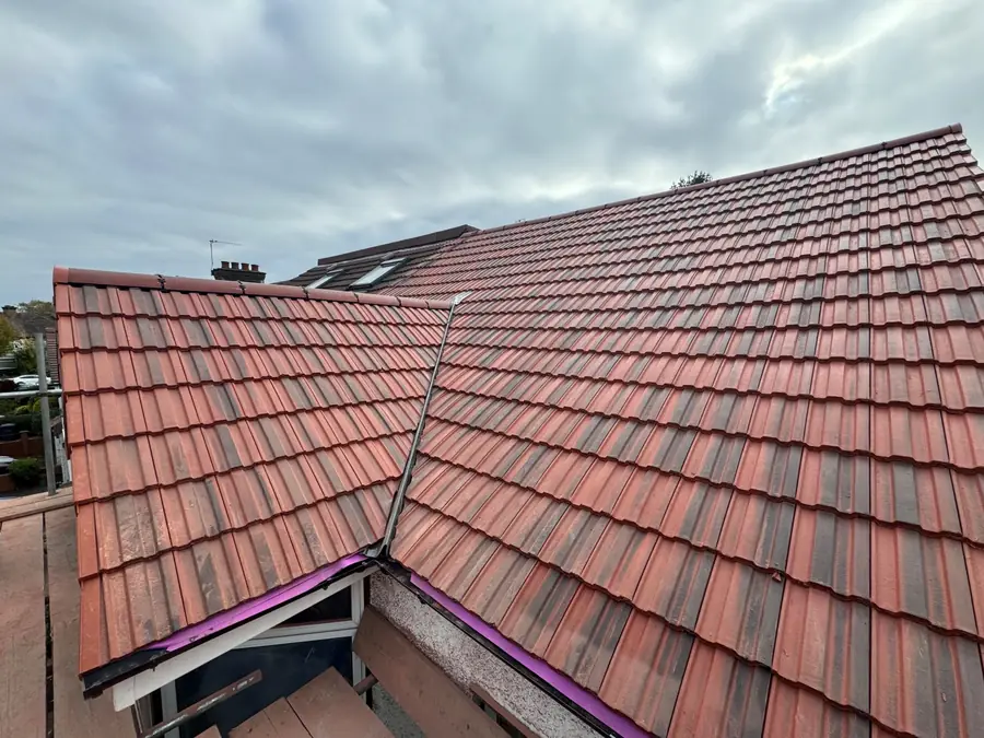 Finished red tiled roof with a dormer and a valley, new purple membrane edge visible at the eaves