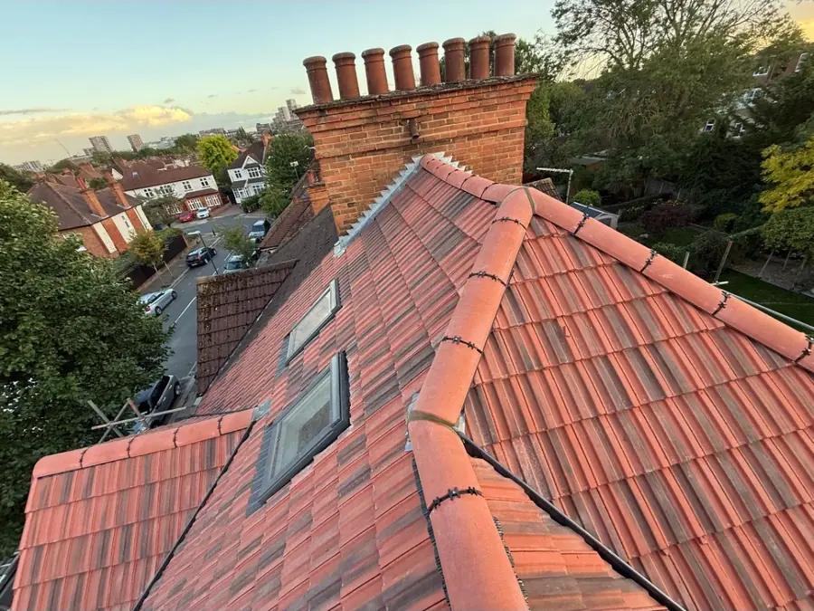 Red tiled roof with two roof windows below a tall brick chimney stack