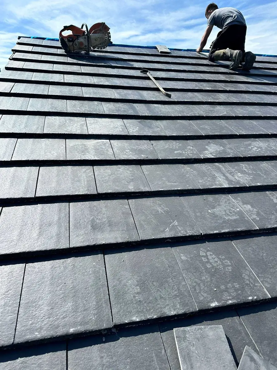 Roofer laying new grey tiles over battens on a pitched roof
